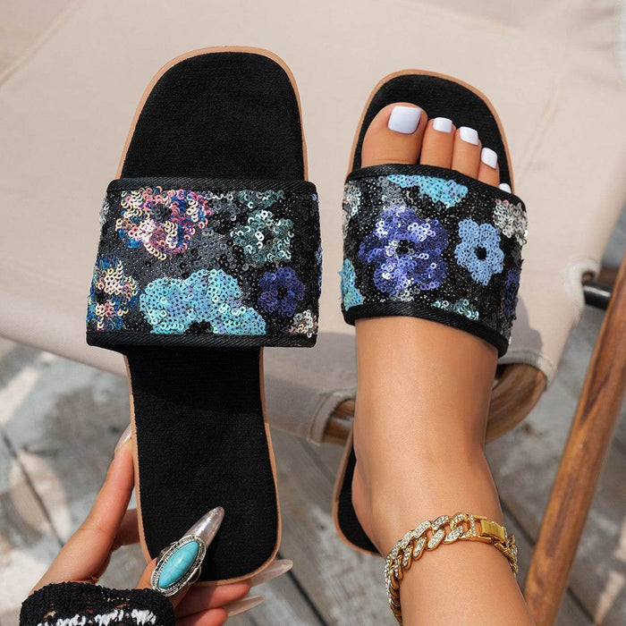 Black slides with floral sequin design worn by a person.