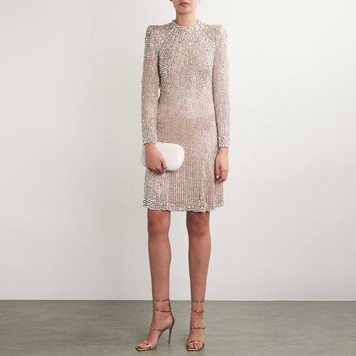 Woman wearing a sparkly dress holding a clutch against a plain background