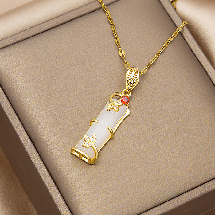 A gold pendant necklace with a white cylindrical stone and small red gemstone accents, displayed on a beige jewelry box.