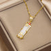 A gold pendant necklace with a white cylindrical stone and small red gemstone accents, displayed on a beige jewelry box.