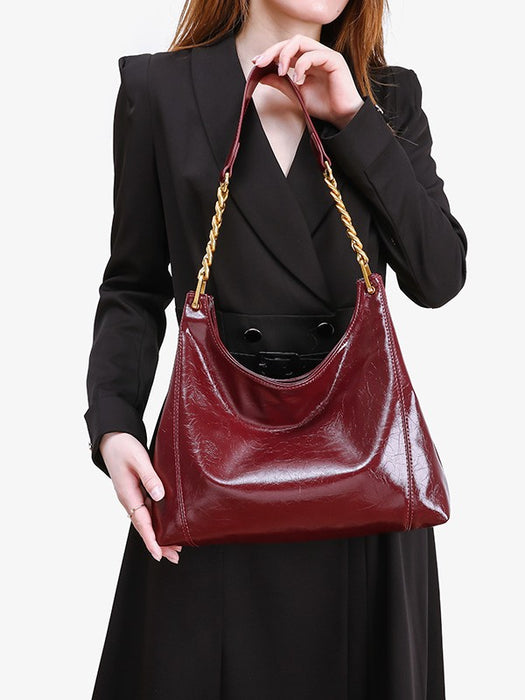 Person holding a burgundy handbag with gold chain strap against a plain background