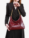 Person holding a burgundy handbag with gold chain strap against a plain background