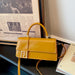 A mustard yellow faux leather handbag with a top handle, a front flap featuring a gold-tone double-F logo, and a matching shoulder strap, styled on a dark table next to a framed print and a magazine.