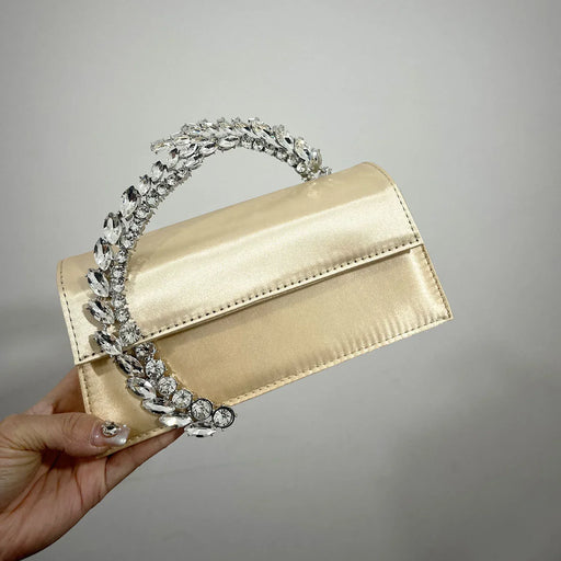 Gold handbag with decorative handle held by a hand against a gray background