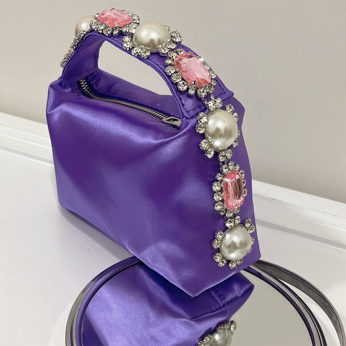 Purple handbag with decorative pearls and gemstones on a white surface