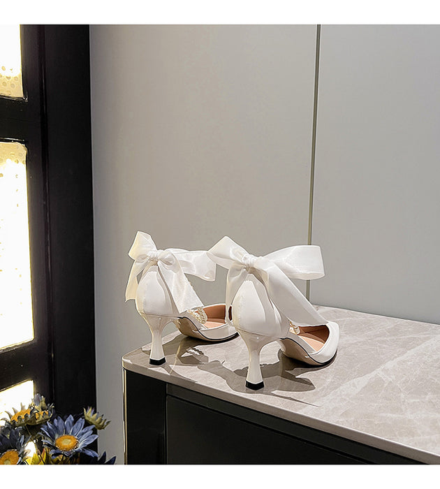 White high-heeled shoes with large bows on a light surface.