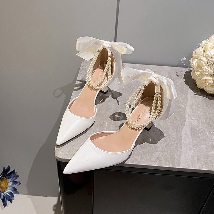 White high-heeled shoes with bow and pearl details on a gray surface.