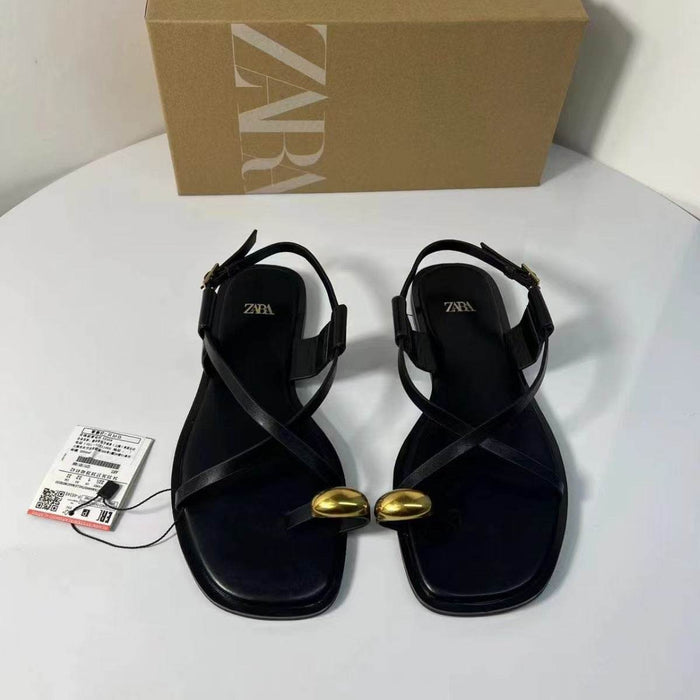 Black sandals with gold accents and Zara box on a white surface