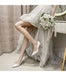 Person in a wedding dress holding a bouquet, wearing white high heels, with a neutral background.