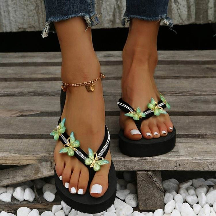 Black sandals with green floral decorations on a wooden floor.