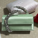 Green handbag with a decorative chain on a textured surface