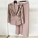 Pink suit with floral embroidery on a hanger against a white wall.