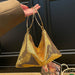 A gold sequined slouchy shoulder bag with double metallic gold handles, held by a hand wearing a brown sleeve against a dark paneled background.