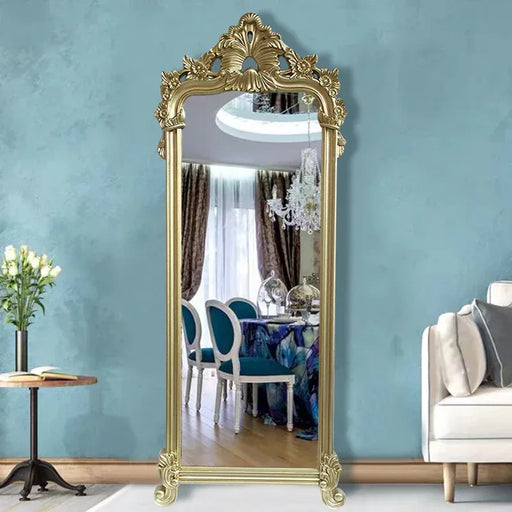 Decorative gold-framed mirror in a room with a blue wall, table, and chair.