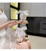 White high-heeled shoes with ribbons held by a person in a white dress.
