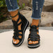 Black strappy sandals worn with ripped jeans on a neutral background