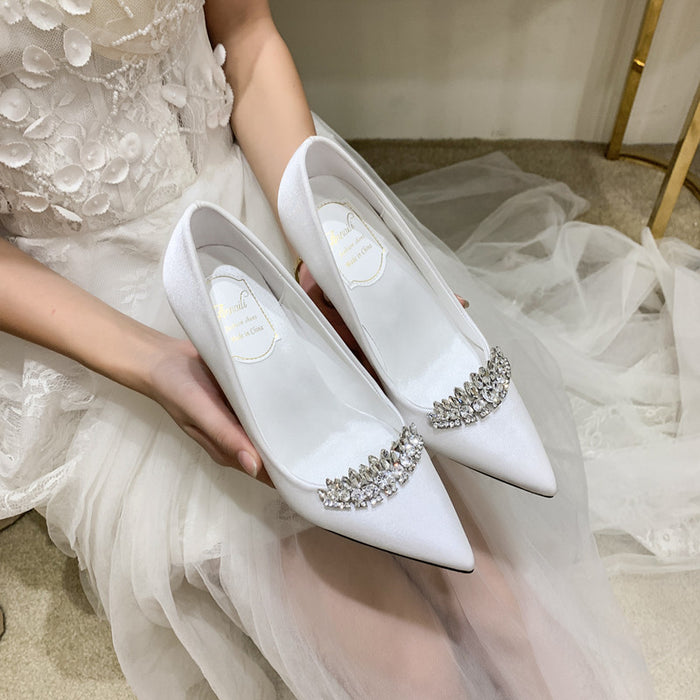 White wedding shoes with embellishments held by a person in a white dress.