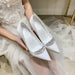 White wedding shoes with embellishments held by a person in a white dress.