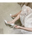 White high-heeled shoes worn with a lace dress on a neutral background