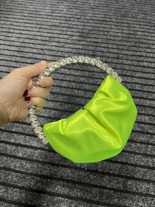Hand holding a green satin bag with a beaded handle on a textured gray background