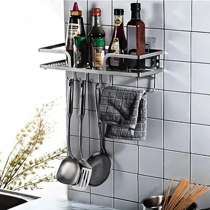 Wall-mounted kitchen organizer with bottles, utensils, and a towel on a tiled wall.