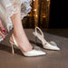 White high-heeled shoes with embellishments worn by a person in a white lace dress.