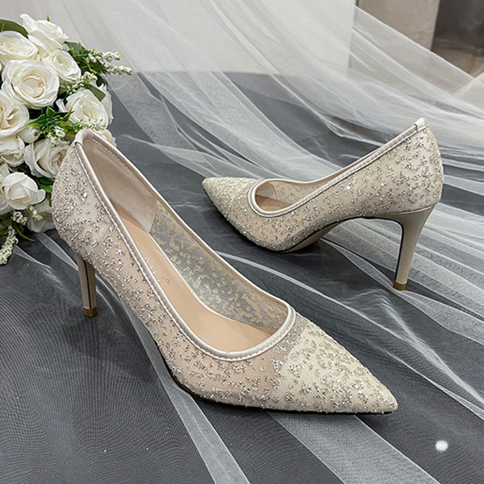Pair of glittery high-heeled shoes on a gray fabric background with white flowers.