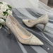 Pair of glittery high-heeled shoes on a gray fabric background with white flowers.