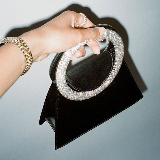 Black clutch with a sparkling handle held by a hand against a neutral background