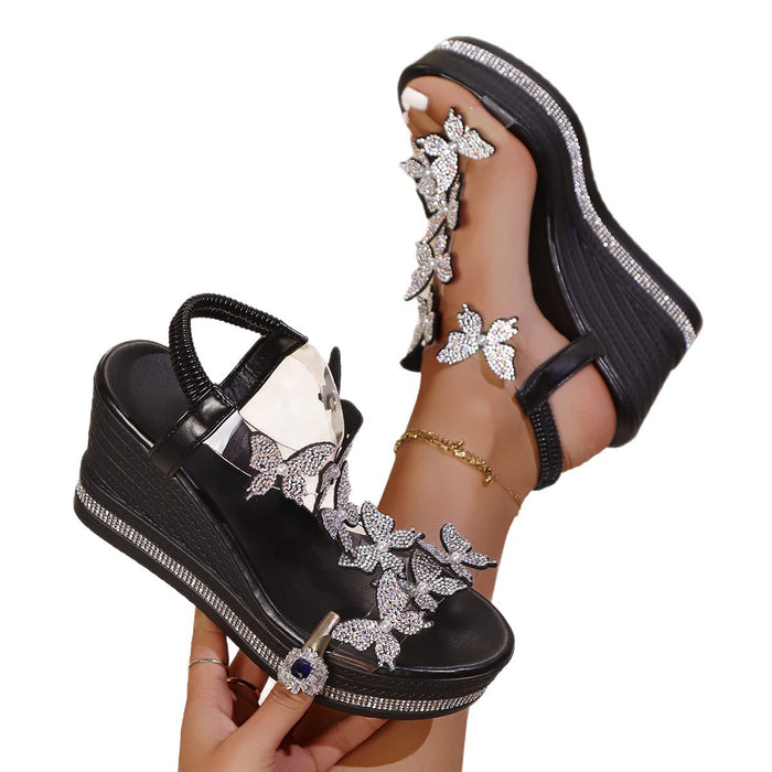 Black wedge sandals with silver floral embellishments on a white background