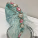 Teal handbag with pink gemstones and white feathers on a white surface