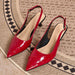 A pair of glossy red slingback pointed-toe pumps with low block heels, displayed on a textured beige and black patterned rug.