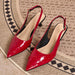 A pair of glossy red slingback pointed-toe pumps with low block heels, displayed on a textured beige and black patterned rug.