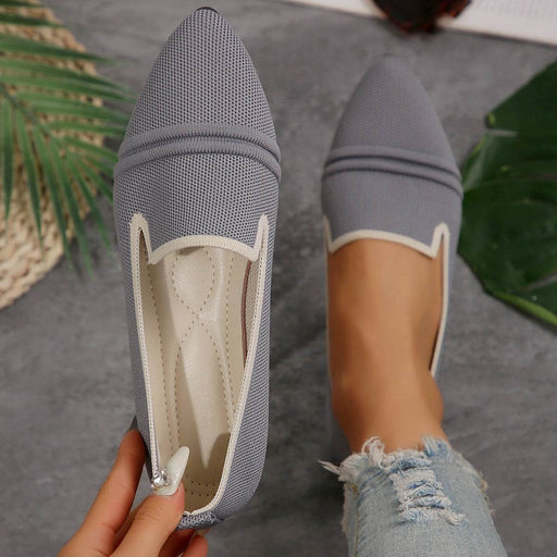 Gray pointed-toe flats with white lining held by a hand on a gray surface.