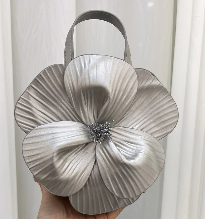 Silver handbag with a large floral design held against a white background