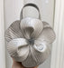 Silver handbag with a large floral design held against a white background