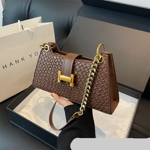 Brown handbag with gold chain and 'H' logo held by a person, with a 'THANK YOU' bag in the background.