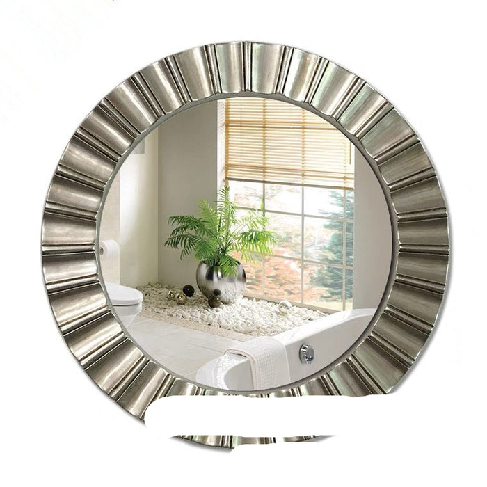 Round wall mirror with decorative silver frame reflecting a bathroom interior.