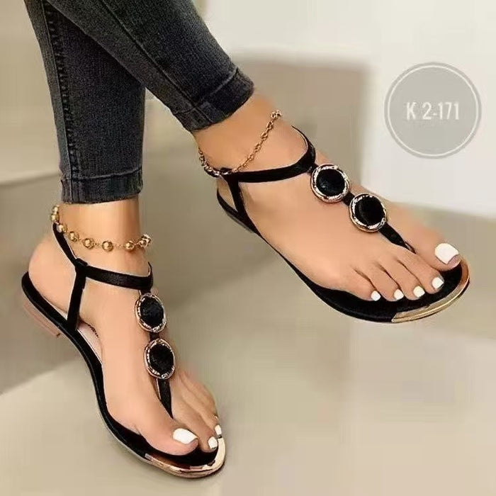 Black sandals with gold accents worn by a person on a neutral background