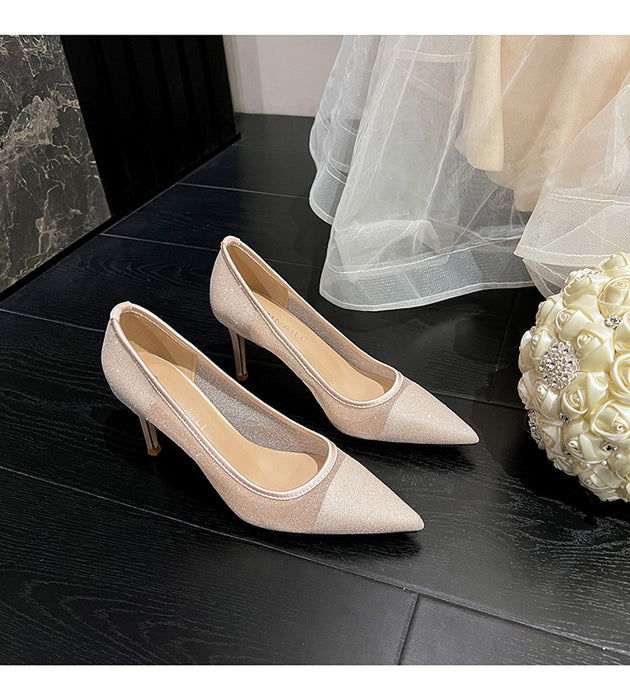 Beige high-heeled shoes on a dark surface with a white flower arrangement.