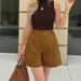 Person wearing a brown sleeveless top and mustard yellow shorts, holding a brown handbag.