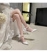 White high-heeled shoes with bow details worn by a person sitting on a chair.
