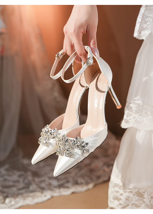 White high-heeled shoes with embellishments held by a person in a wedding dress.