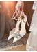 White high-heeled shoes with embellishments held by a person in a wedding dress.
