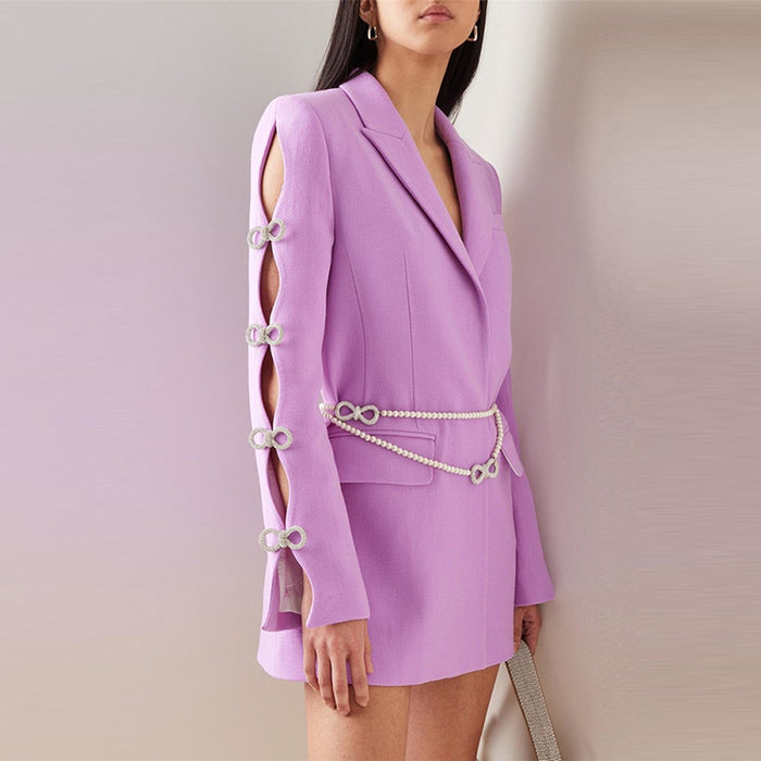 Woman wearing a lavender blazer dress with cut-out sleeves and pearl embellishments on a plain background