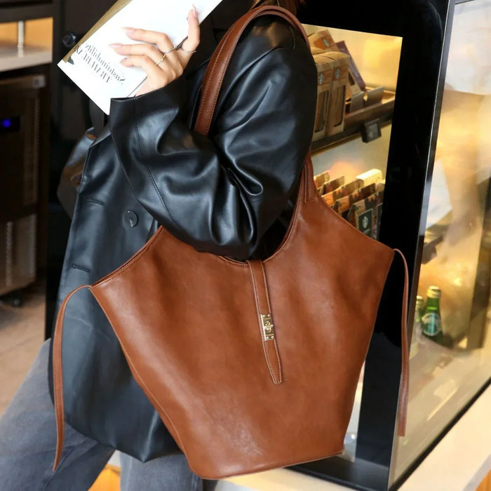 Brown leather handbag held by a person wearing a black coat in an indoor setting.