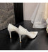 White high-heeled shoes on a dark wooden floor with a draped white fabric in the background.