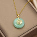 Gold chain necklace with a round light green jadeite pendant featuring a gold Chinese character charm, displayed on a beige jewelry box.