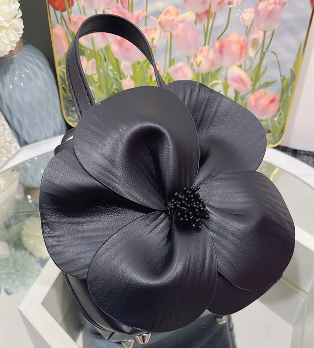 Black flower-shaped handbag on a white surface with a blurred floral background