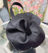 Black flower-shaped handbag on a white surface with a blurred floral background